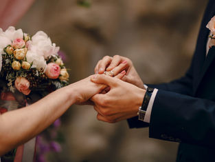 Bride and groom exchanging wedding rings Sri Lanka during the ceremony, with a pink and white bridal bouquet in the background