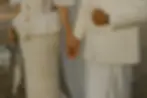 wedding theme sri lanka 01: Close-up of a couple holding hands; both wearing intricate white attire. The woman holds a bouquet, conveying a wedding or formal setting.