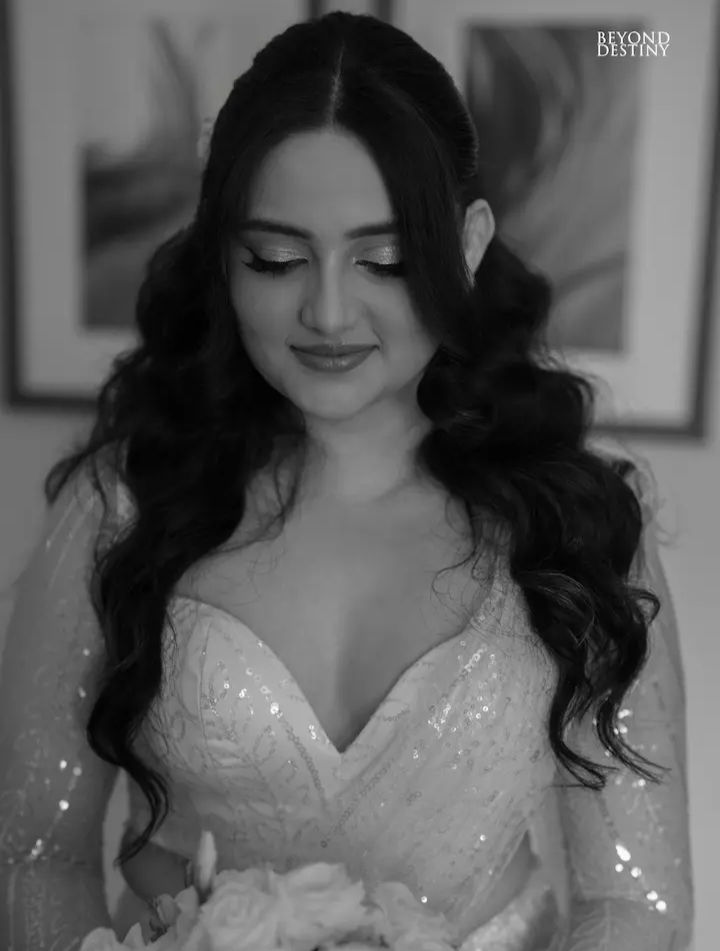Woman in a sequined dress holds flowers, eyes closed, smiling softly. Black and white with art in background.