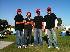 A photo of four male GUAC Taco Employees, all dressed in Black shirts, blue jeans, and red hats