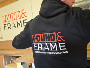 Installation expert in ground screws vs concrete with "FOUND & FRAME" logo in orange and white; indoor setting with a workshop table and logo on the wall.