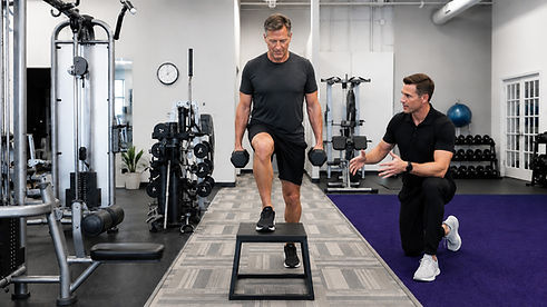 Starck Fitness personal trainer coaching a man in his 40s through a lower-body strength exercise in a clean Naperville gym.
