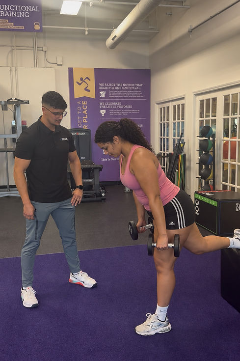 Starck Fitness personal trainer observing a woman’s form during a dumbbell exercise with her rear foot supported in a Naperville gym.