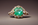 Gold ring with a large green gem surrounded by smaller diamonds on a smooth, brown surface. The setting is elegant and luxurious.