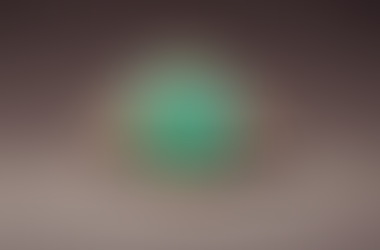 Gold ring with a large green gem surrounded by smaller diamonds on a smooth, brown surface. The setting is elegant and luxurious.