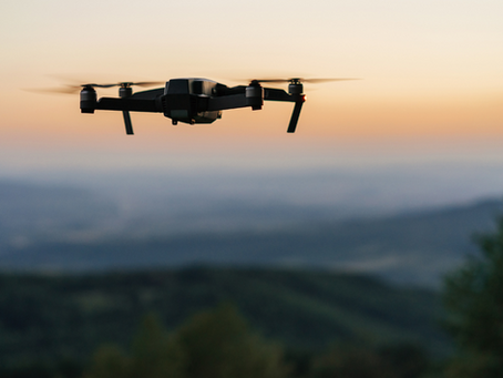 Drone flying at sunset over a blurred, wooded landscape. The sky is orange, creating a calm and serene mood.