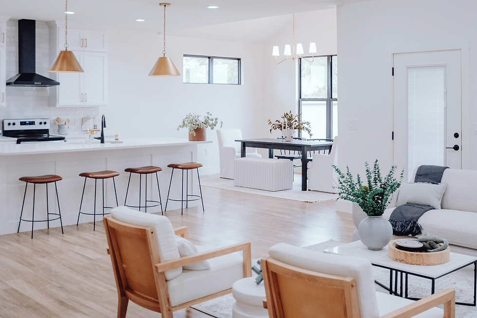 Bright modern open-plan kitchen and living room with white walls, wood bar stools, black table, and potted plants.