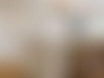 Elegant white kitchen with island, wooden bar stools, modern chandeliers, and a window view. Warm lighting enhances a cozy ambiance.