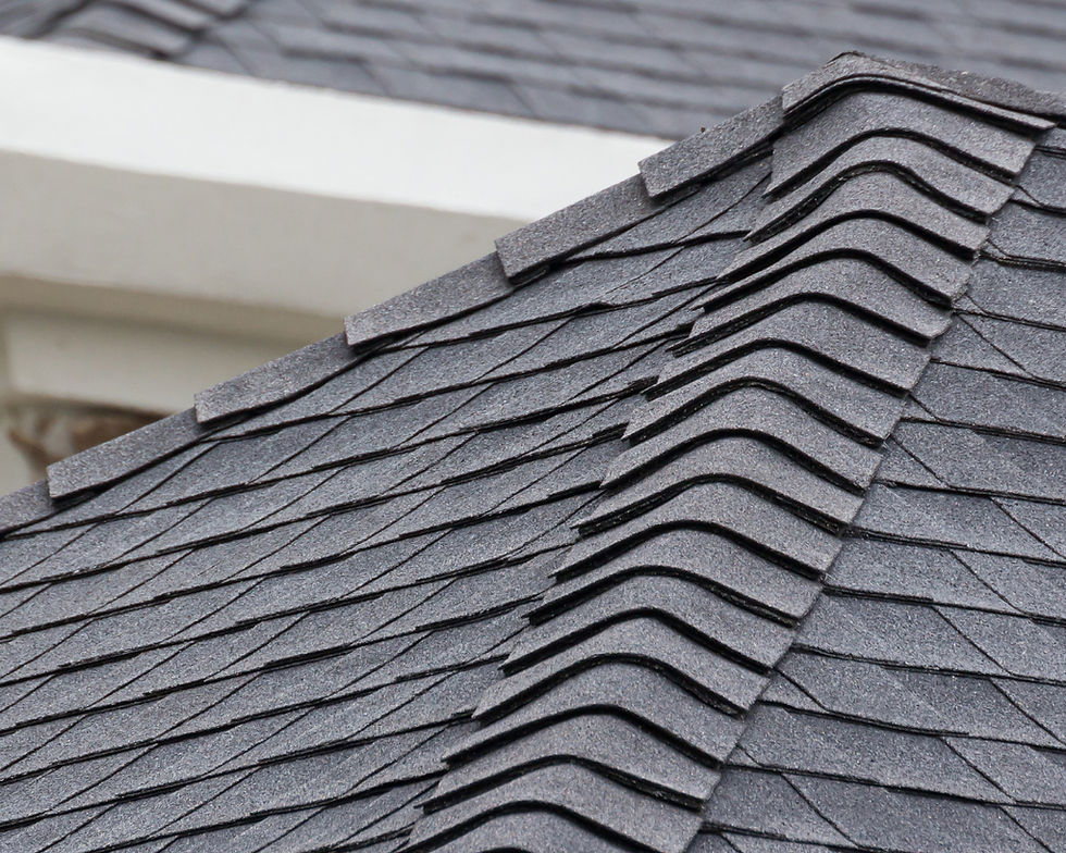Close-up of gray asphalt roof shingles layered neatly. The texture is coarse, with visible lines and patterns. Background shows white trim.