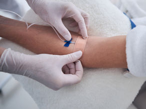 A photo of a docotor's gloved hands taping down an IV needle in the arm of a patiend