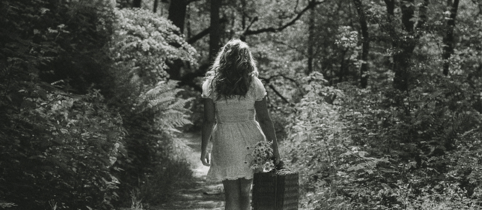 Black and white photo of a Wild Woman walking away through woodlands, symbolising a healing journey in nature.