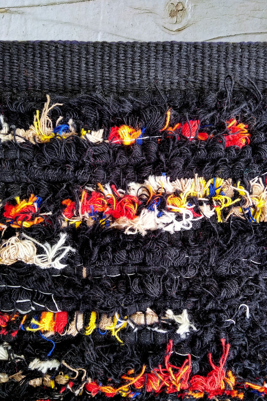 Hem of black handwoven rug with red, white, and yellow accents