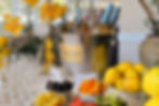 Chilled champagne bottles in a bucket, surrounded by yellow orchids, lemons, fruit bowls, and glasses on a table. Bright and festive setting.