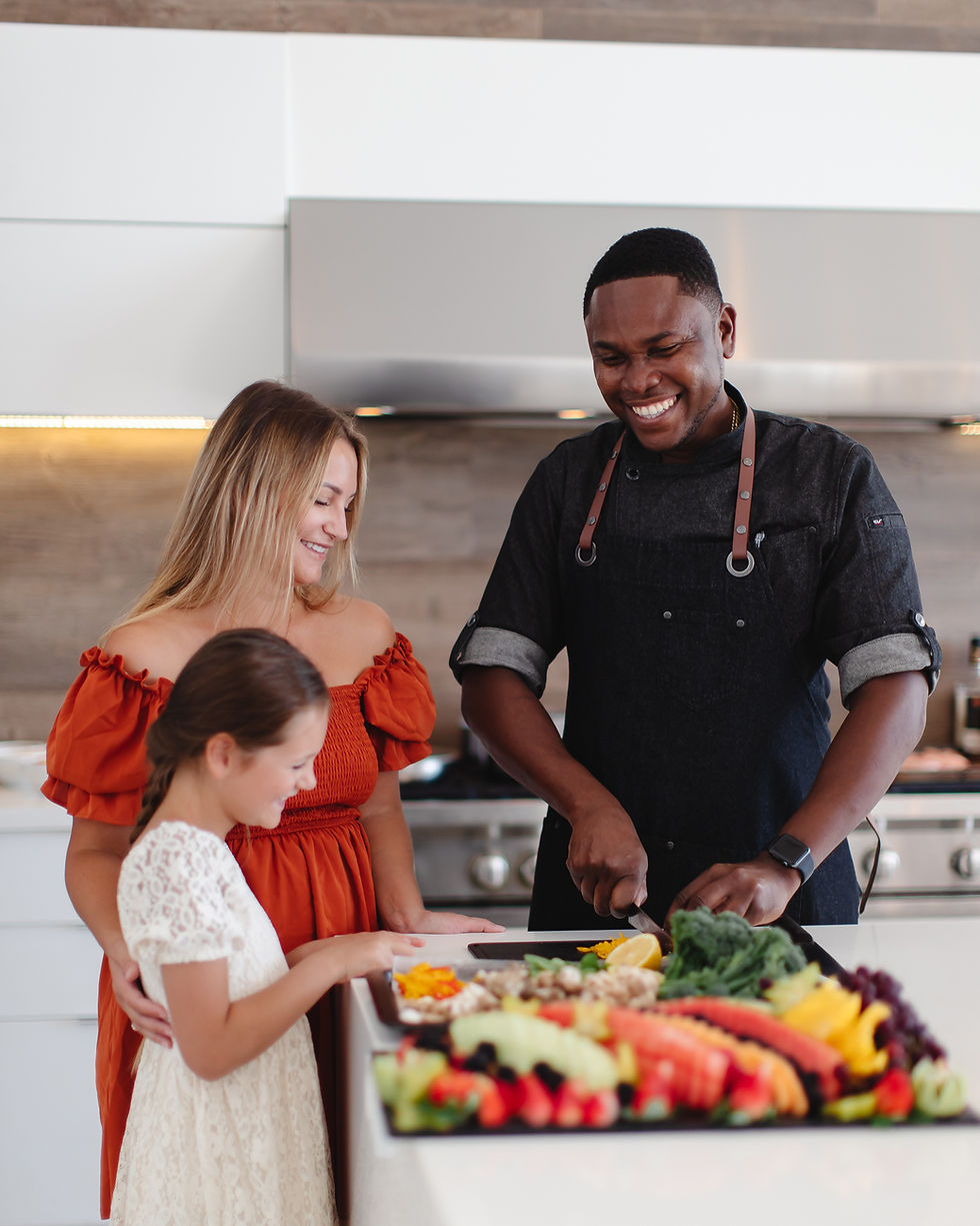 A woman and her daughter stand in a modern Beach Enclave Villa with a talented chef who is preparing a fresh vegetable dish for dinner.