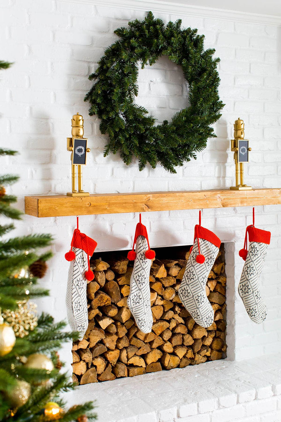 A white Christmas holiday fireplace with a mantel decorated with a green wreath, nutcrackers and stockings for a stylish and cozy feel.
