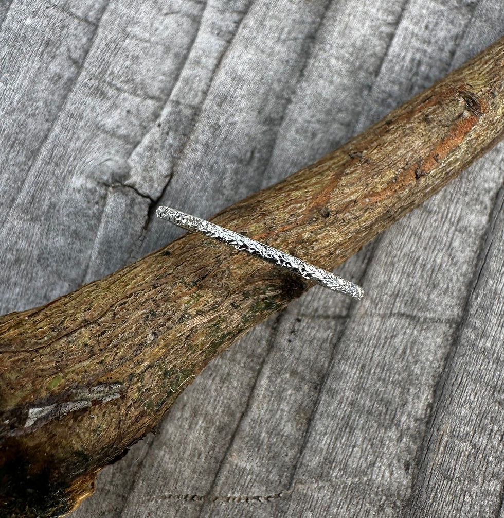 Textured sterling silver ring on a stick laying on a wooden bench