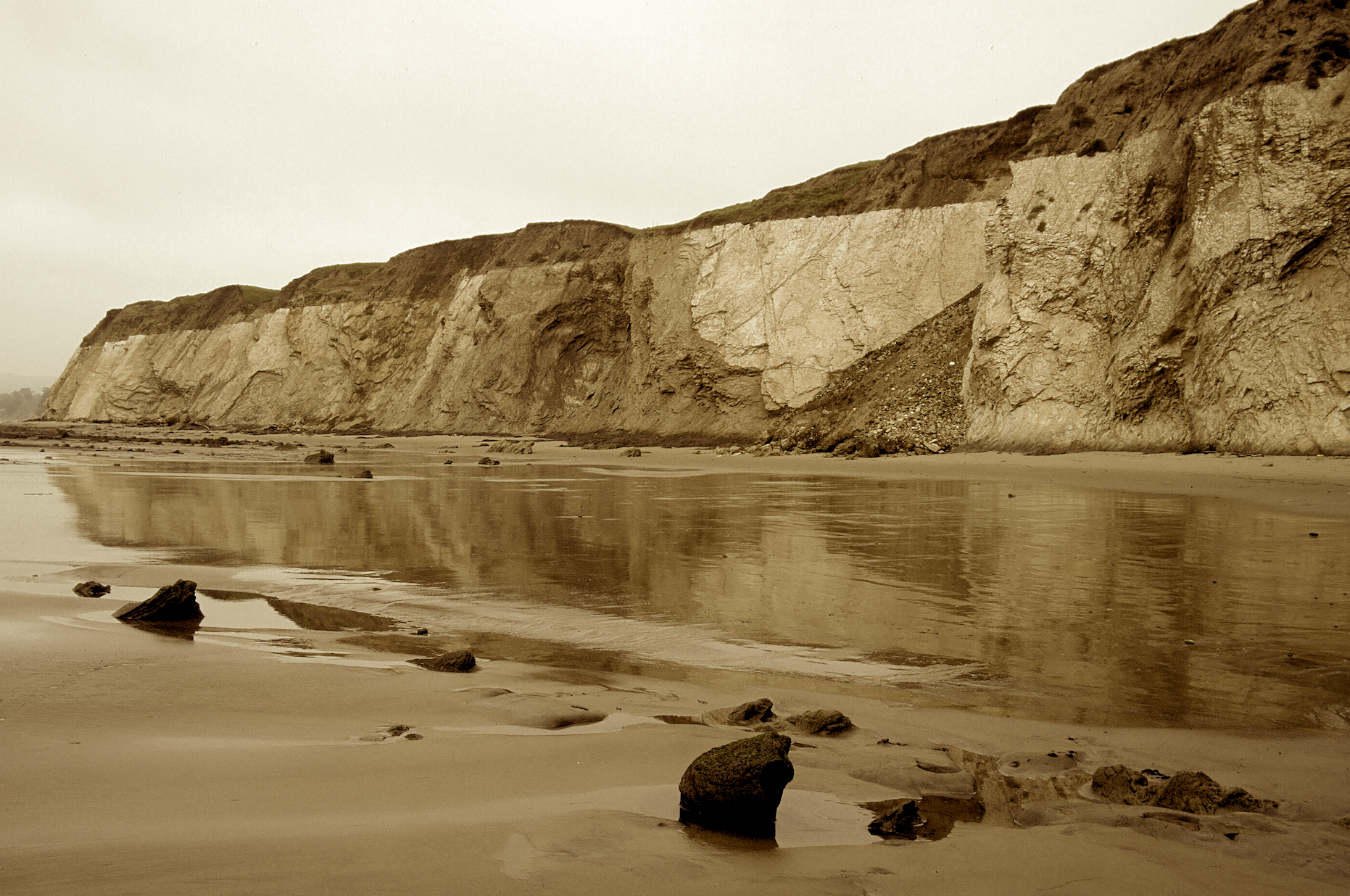 Sepia colored photo of tall bluffs towering over the California coastline in Goleta.