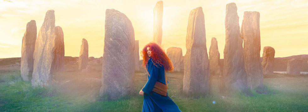 A photograph of a Disney's Brave inspired photograph shot in Stornaway Hebrides Scotland for Disney 100 Landmark campaign by Linda Blacker. Our model wears a blue and has flaming red curly hair, standing in front of the  Callanish Standing Stones, which inspired Brave.