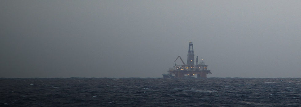 Plataforma de petróleo isolada no horizonte do Mar do Norte, ao largo da Escócia, com as luzes acesas sob céu cinzento e mar agitado
