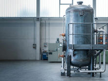 Vaso de pressão vertical em planta industrial iluminada, com plataforma de inspeção e tubulação conectada.