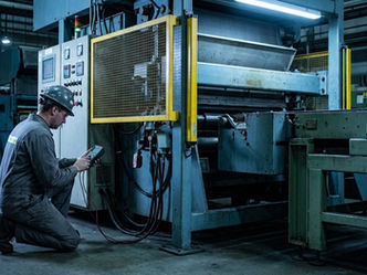 Técnico com instrumento de medição em frente a uma máquina industrial com proteção instalada