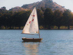 Small sailboat with a full white sail on a lake surrounded by mountains
