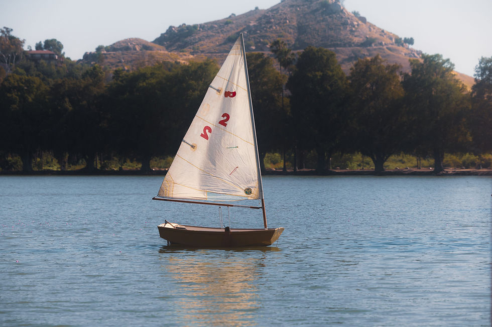 Small sailboat with a full white sail on a lake surrounded by mountains