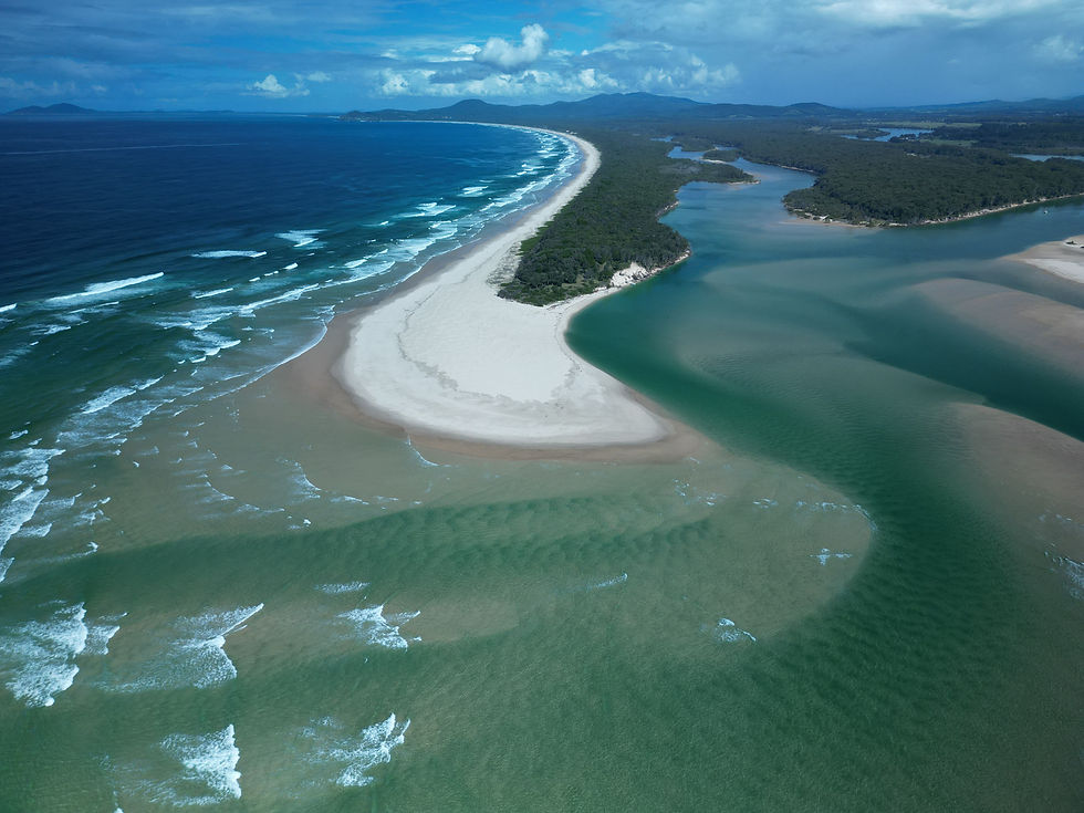 Aerial view of ocean waves beside a winding river and sandy beach