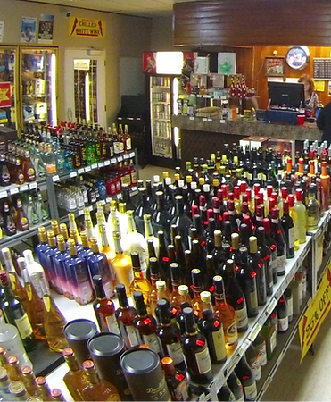 Shelves of liquor bottles inside a store, person at counter.