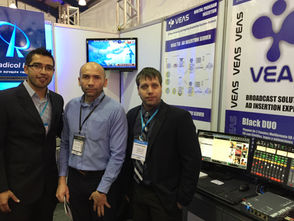 Three men standing at the Veas.tv booth during a trade show.