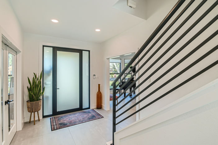 Modern entryway with black-framed front door, staircase, and natural styling.