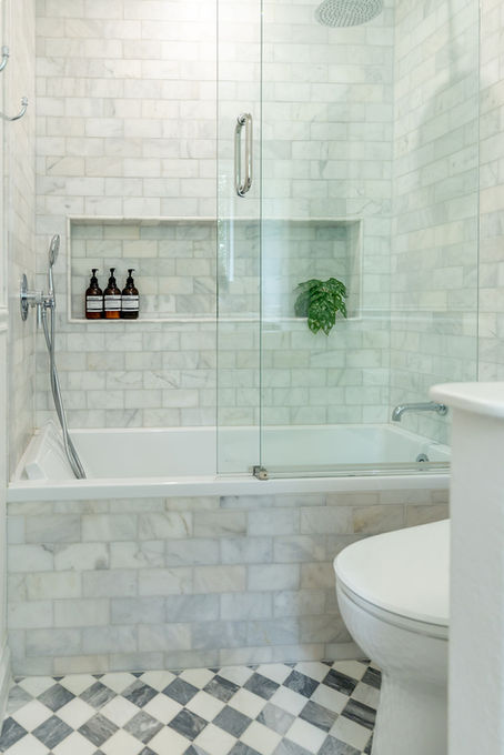 Children's bathroom with glass shower enclosure, marble tile, and built-in shower niche.