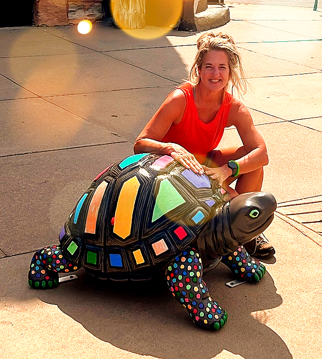 Woman poses with a large, colorful turtle sculpture on a sidewalk