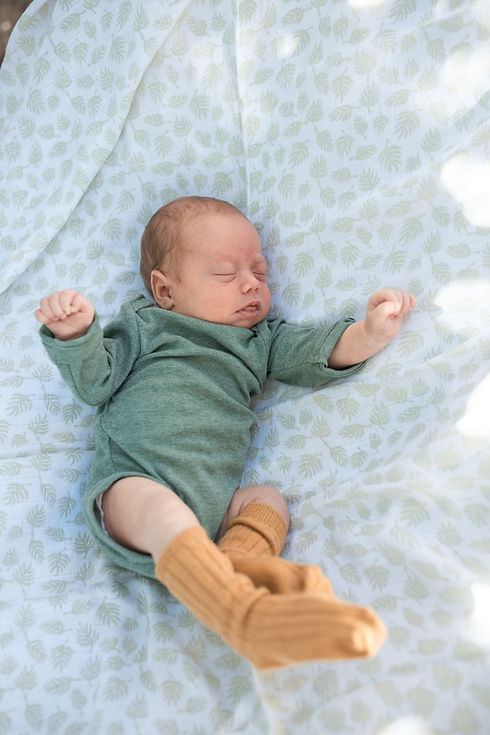 Baby mit Body liegt auf einer Decke