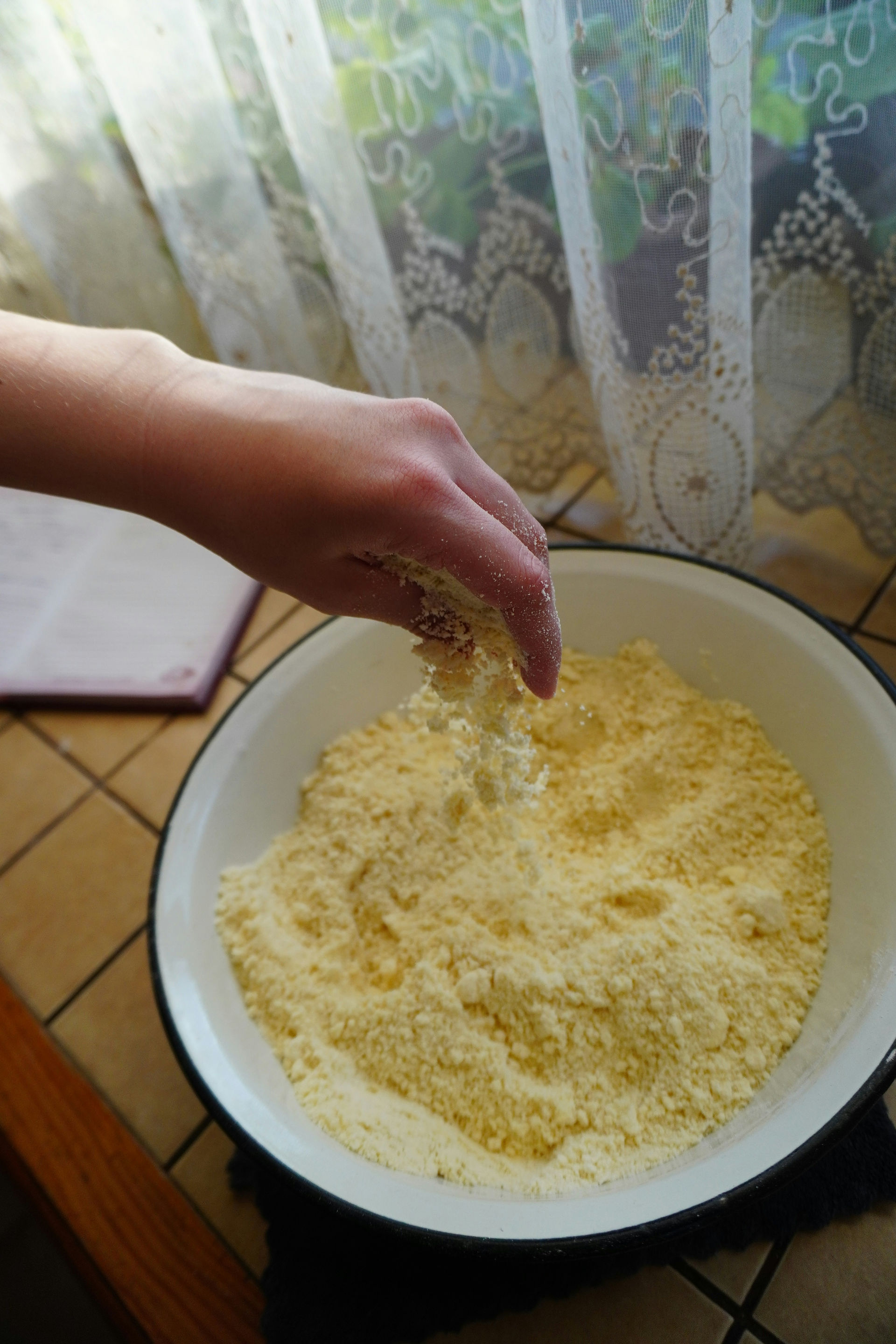 Eine Hand bearbeitet eine krümelige Mehlmischung in einer Schüssel; Foto zur Veranschaulichung.