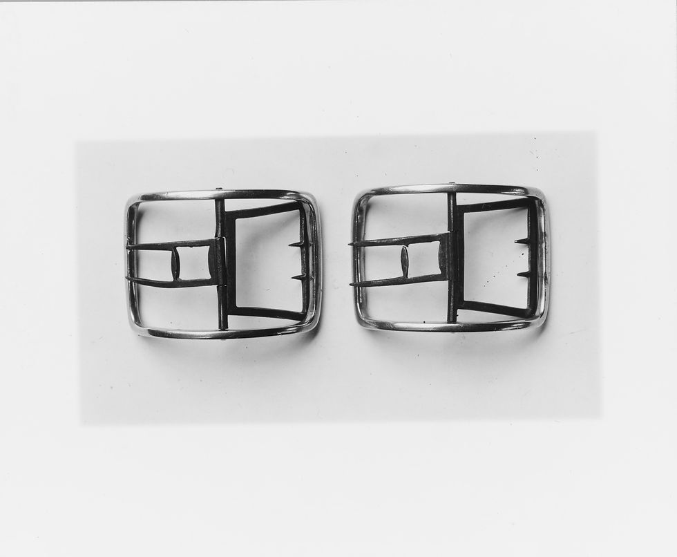 Dos hebillas de zapato de plata sin adornos, con marcos curvos, fotografiadas juntas.