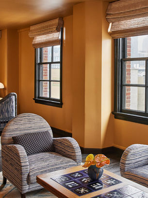Ochre-walled guestroom at Downtown L.A. Proper with striped armchairs, a patterned bed and black-framed windows.