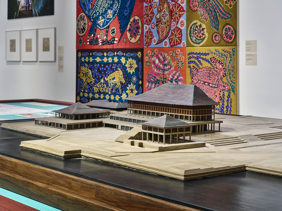 Exhibition view at Vitra Design Museum, 2026: an architectural model on a display table in front of a vividly patterned textile.