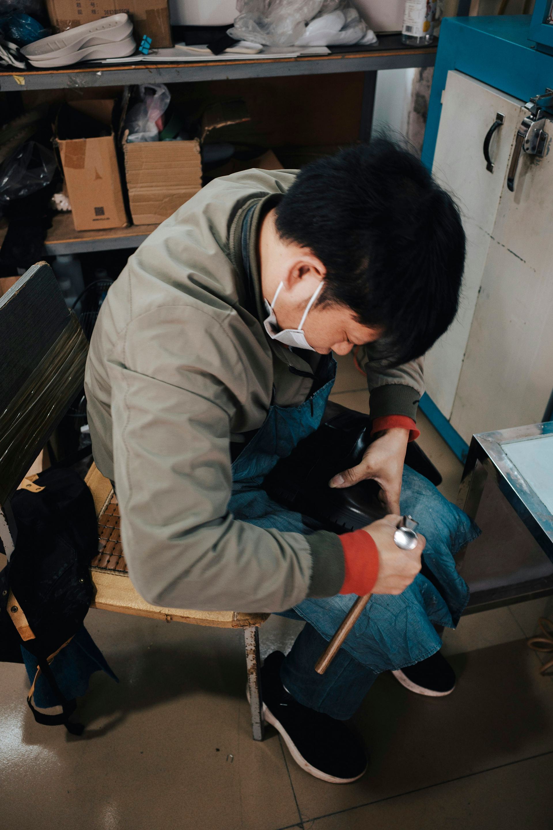 Ein sitzender Arbeiter hält einen schwarzen Stiefel und einen Hammer in einer Schuhmacherwerkstatt.