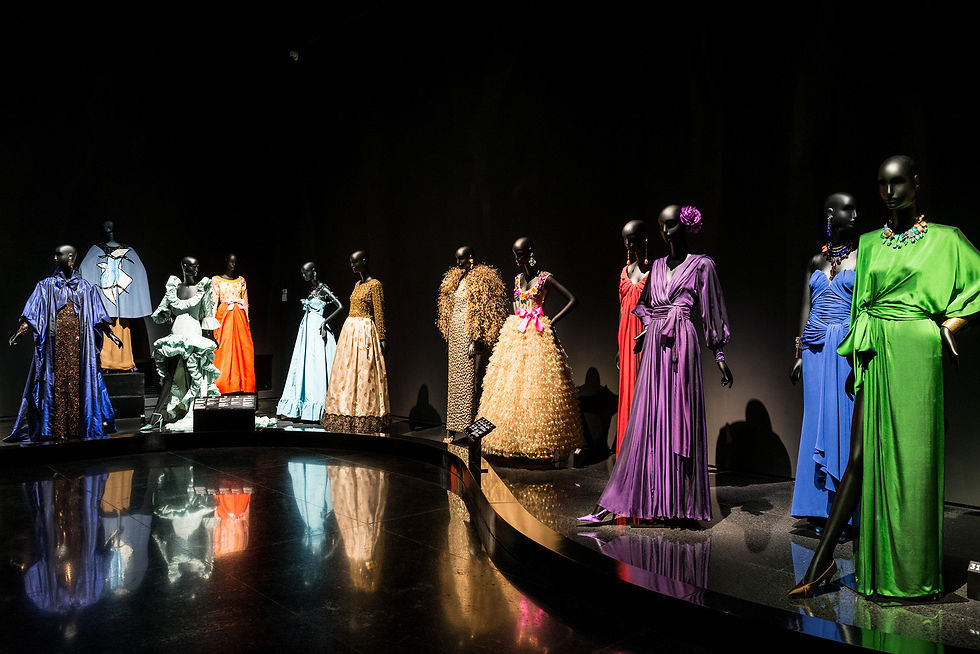 Colourful dresses arranged along a curved display in the black exhibition gallery.