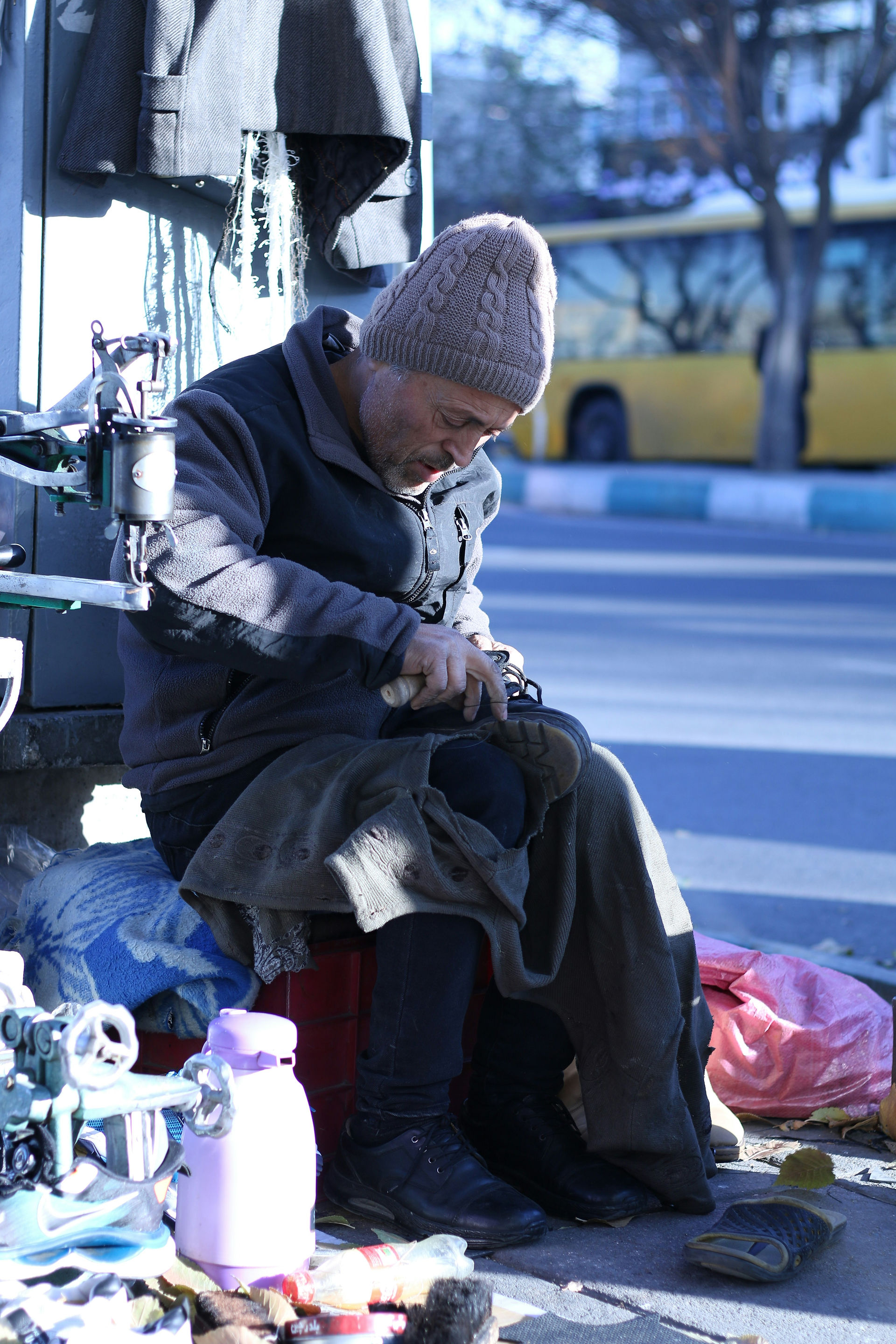 Ein Schuhreparateur am Straßenrand arbeitet in Teheran an einem dunklen Schuh neben einer Nähmaschine.