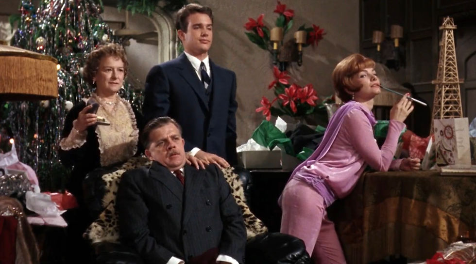 Four people in a festive room with a decorated Christmas tree. One woman in pink poses playfully with a cigarette holder. Others appear relaxed. Joanna Roos, Pat Hingle, Warren Beatty, and Barbara Loden are one unhappy family in the classic 1960s Hollywood film romance movie about sex and repression, "Splendor in the Grass"