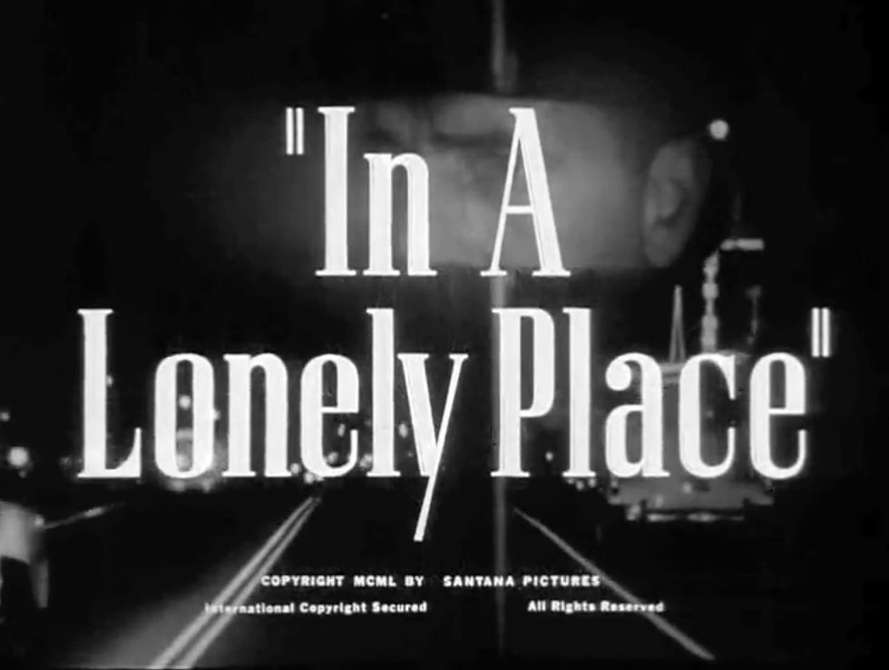Text "In A Lonely Place" over a dark road with blurred lights. A faint face is visible. Moody and noir-like atmosphere. Opening title credit in the classic Hollywood movie romance Nicholas Ray film noir "In a Lonely Place"