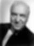 Elderly man in a suit smiling warmly; black and white portrait with subtle lighting, plain background, conveys a friendly, composed mood. Hollywood TV and movie actor star portrait photo of William Frawley