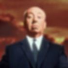 A person in a dark suit stands with a serious expression against a dramatic sunset backdrop with orange and yellow clouds. Color portrait photo of British Hollywood film director movie star Alfred Hitchcock