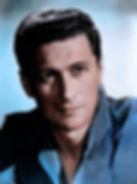 A man with dark hair in a blue shirt gazes thoughtfully off-camera. The background is a soft blend of blue and white hues. Color portrait photo of Italian European Hollywood movie star leading man young Cesare Danova