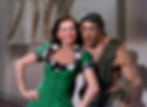 Smiling woman in a green dress with plaid trim poses with a Hercules pithecanthropus erectus statue in a Natural History museum. Dinosaur bones visible in the background. Ann Miller sings and dances to Prehistoric Man in the classic movie Hollywood MGM musical film On The Town