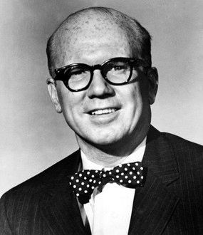 Bald man wearing glasses and a polka dot bow tie smiles against a plain background. Black and white image with a cheerful expression. Portrait photo of actor, Hollywood movie star, TV film and the voice of Piglet, young John Fiedler
