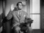 A man in a suit raises his right hand, holding a hat in his left. He appears serious. The setting includes a wooden door and a wall outlet. Joel McCrea stars in the classic Hollywood romantic comedy film rom-com movie 1940s "The More the Merrier".