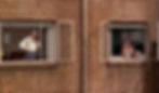 Two windows on a brick wall, man adjusting shirt in one, woman in nightgown in the other. Curtains, paintings visible in rooms. Raymond Burr and Irene Winston are husband and wife in the Alfred Hitchcock classic Hollywood film suspense movie "Rear Window"